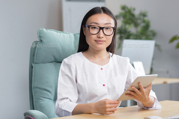 Online admission to the hospital. A young beautiful Asian woman doctor with tablet - Stock Photo - Images
