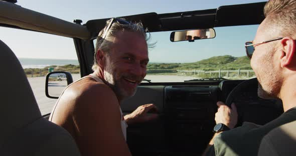 Happy caucasian gay male couple driving car and smiling on sunny day at the beach alt