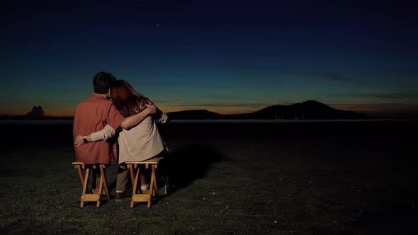 young couple in love sitting and hugging at the grass filed at night
