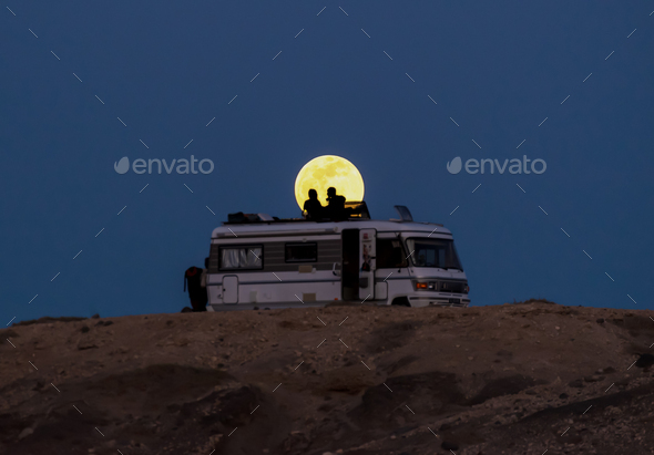 Silhouette of Couple on the Roof of a Motorhome in a Cliff with the Full Moon Behind.Copy Space