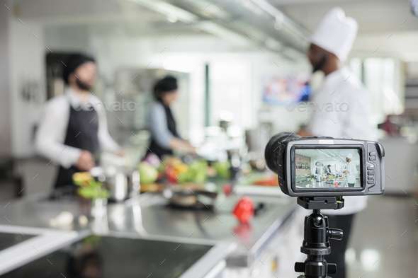 Selective focus of camera filming restaurant kitchen chefs cooking gourmet dish for culinary school