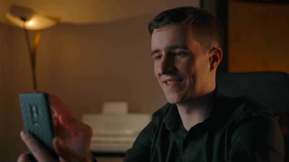 Young Man Communicates Online Via Phone in a Cozy Apartment alt