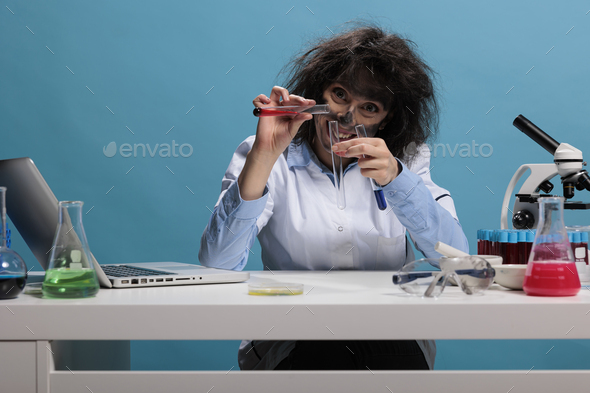 Portrait of crazy chemist with wild look mixing dangerous chemical compounds while sitting at desk