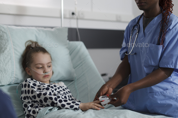 Ill kid sitting in hospital pediatric ward while medical staff monitoring health condition using