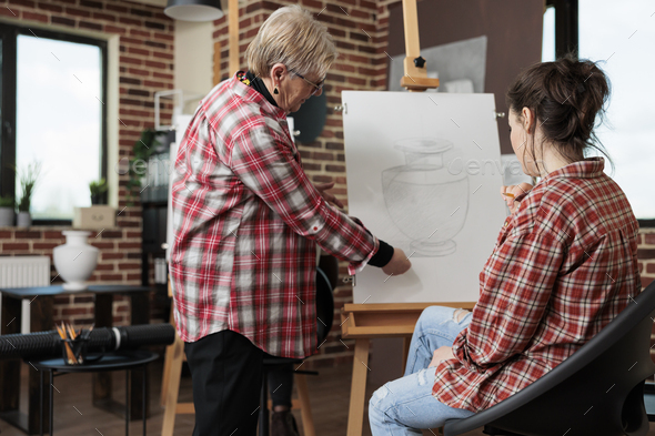 Elderly art teacher showing sketching technique to young artist