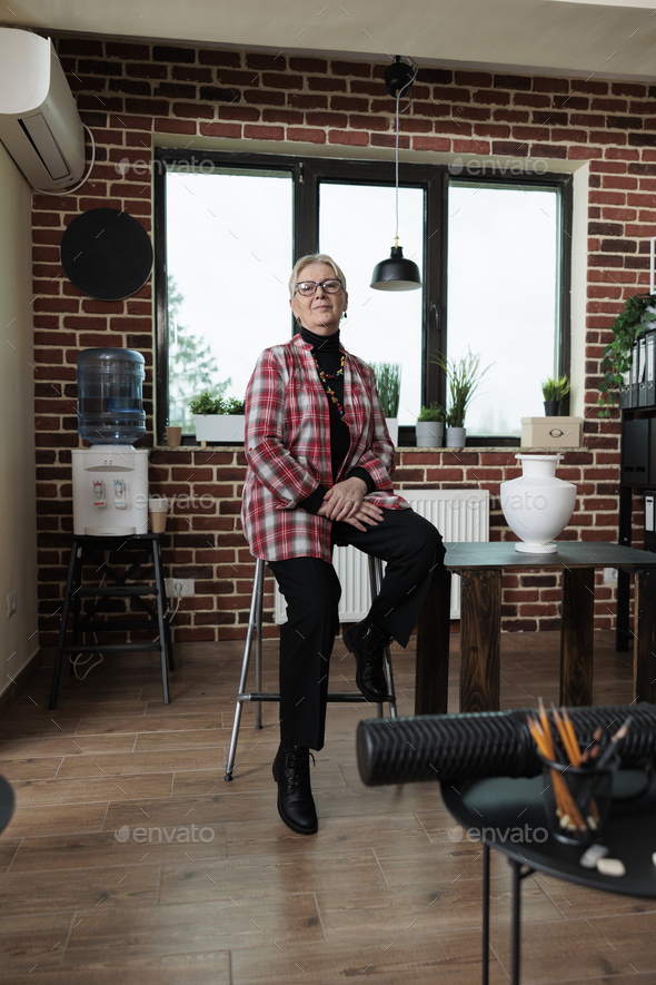 Portrait of elderly artist teacher standing on chair in creativity studio
