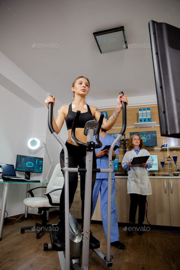 Female athlete who makes a physical effort on the stepper and has electrodes and doctors glued on it