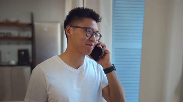 Handsome Young Asian Man Having Phone Call Relaxing Near Window in Living Room alt