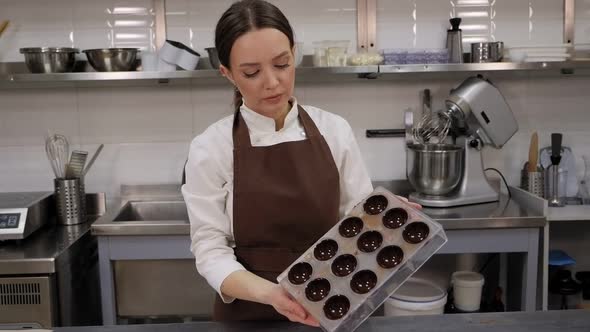 A Female Pastry Chef Holds a Form for Making Praline Chocolates in a Kitchen alt