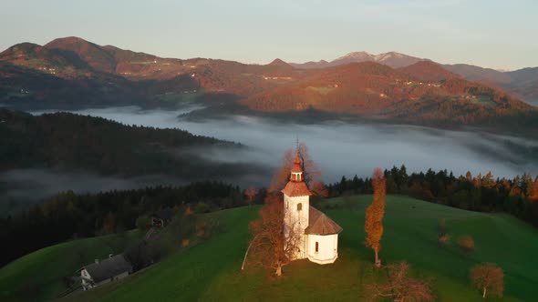 Aerial View of the Hills, Colorful Forest in the Fog and the Church of Sv Tomaz. Sunrise in Slovenia