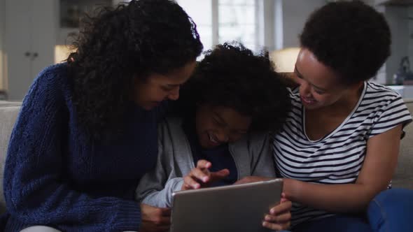Mixed race lesbian couple and daughter using digital tablet on couch laughing alt