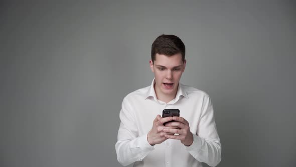 Dissatisfied Guy with a Smartphone in His Hands on a Gray Background