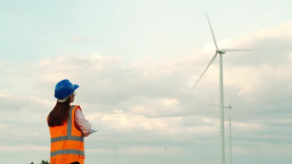 female engineer working and writing on clipboard against wind turbine farm