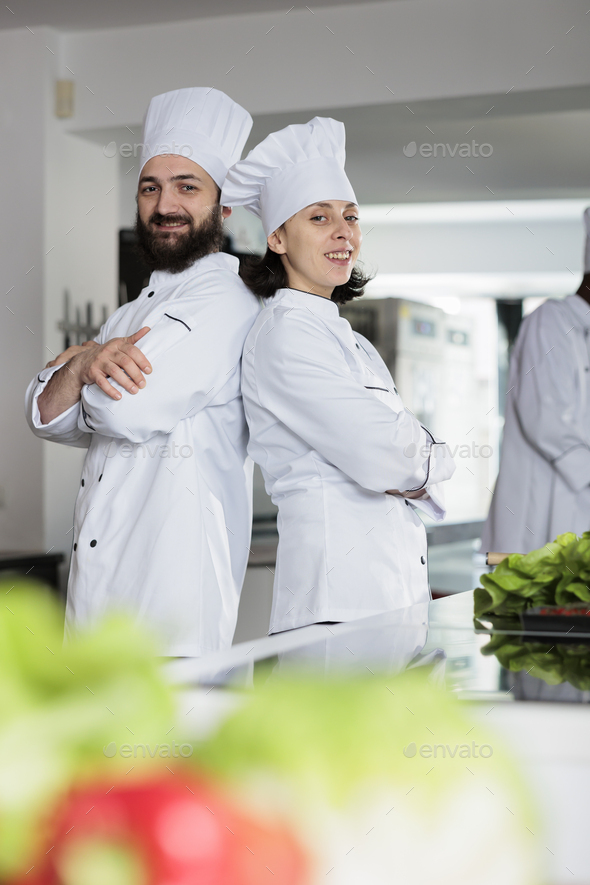 Skilled cooks wearing cooking uniforms while posing back to back in