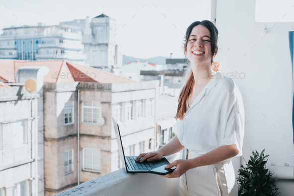 Young woman businesswoman freelancer using laptop for work outdoors on a balcony. Freelance work