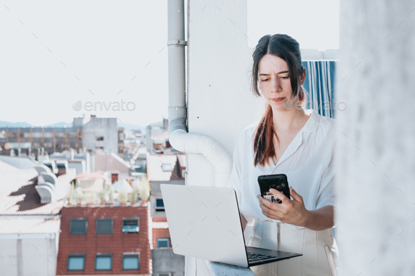 Young woman businesswoman freelancer using laptop,checking phone worried. Freelance work