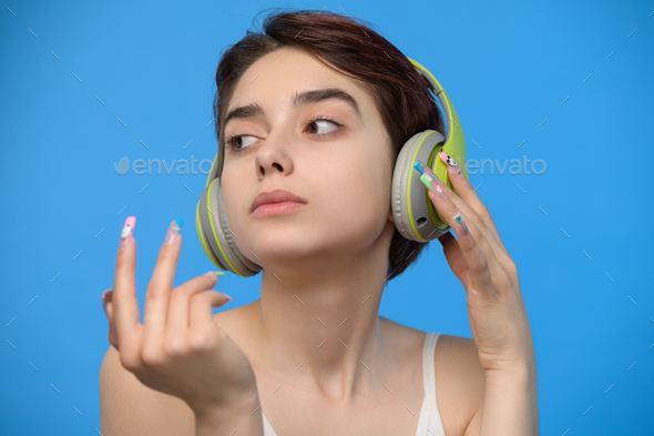 Cute young brunette listening to music using bluetooth wireless headphones