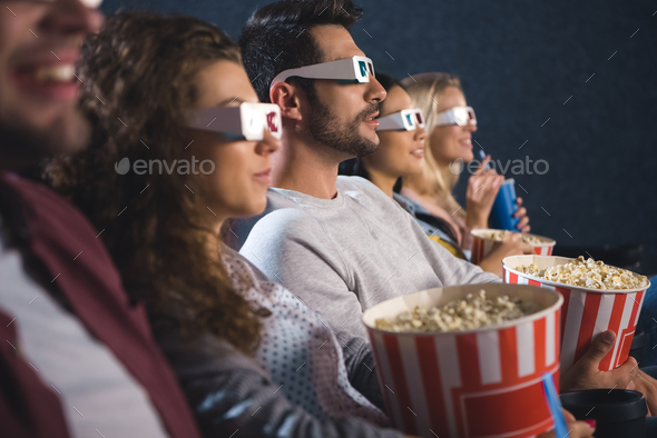 multiethnic friends in 3d glasses with popcorn watching film together in movie theater