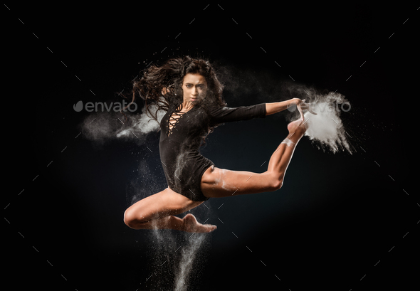 beautiful ballerina in black bodysuit with talc powder jumping on dark background