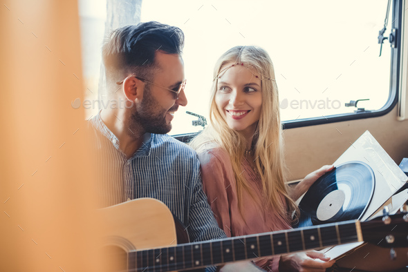 beautiful hippie couple resting inside trailer with acoustic guitar and vinyl record