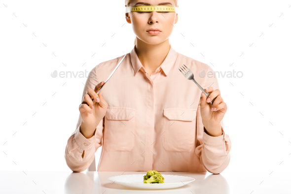 attractive woman with tape measure on eyes ready to eat broccoli isolated on white