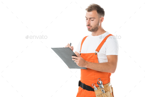 handsome auto mechanic in orange uniform writing something to clipboard isolated on white