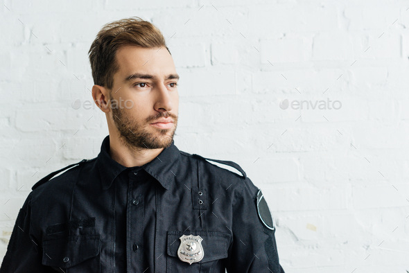 portrait of thoughtful young policeman in front of white brick wall ...