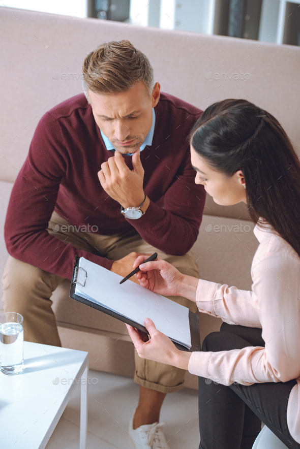 female psychologist pointing at blank clipboard during therapy appointment with male patient