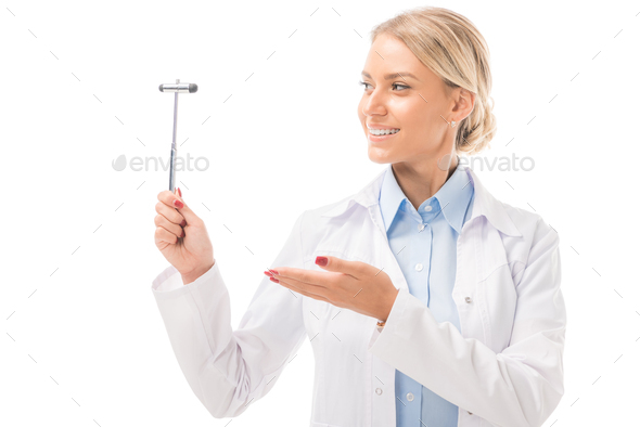 smiling young female neurologist pointing at reflex hammer isolated on white