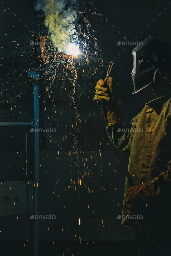 worker in protection mask welding metal at factory