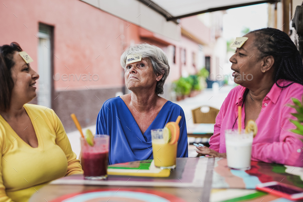 Senior multiracial women having fun playling guess game together at bar outdoor