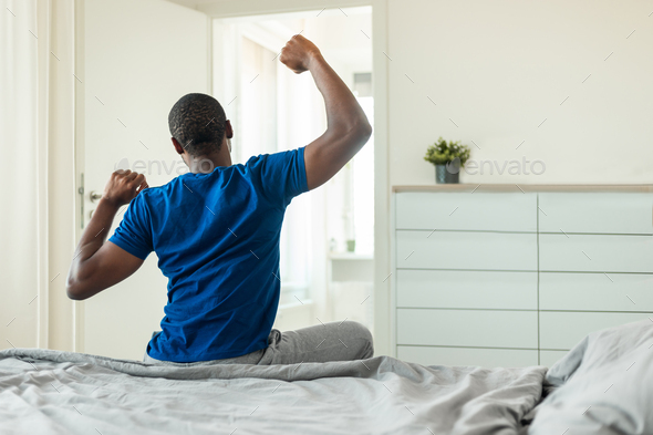 Well-rested Indian Guy in Pajamas Stretching in Bed Stock Photo