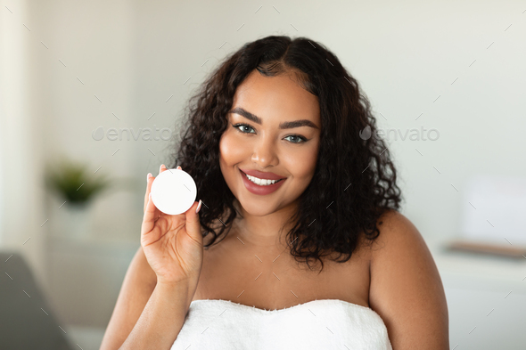 Skin care cosmetics. Black body positive lady holding jar with moisturising cream, advertising