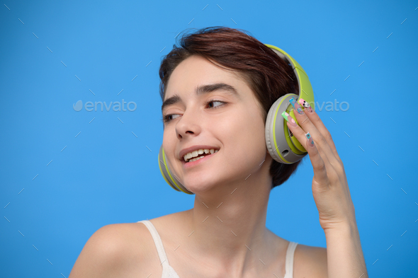 Cute young brunette listening to music using wireless headphones