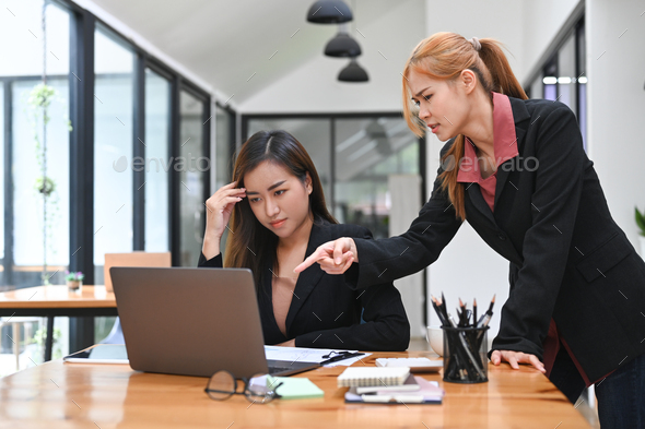 Displeased female boss scolding young intern with bad work results.
