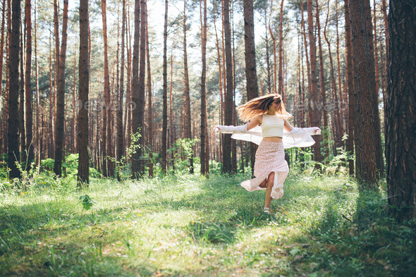 Young beautiful hippie woman walks in the summer forest laughs dances ...