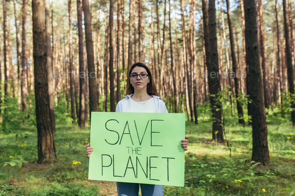 Young female activist standing in the woods with a poster save the planet, a volunteer struggles