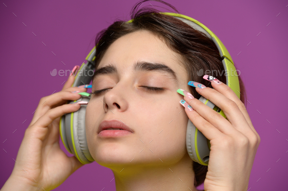 Affectionate pretty girl with short haircut and extravagant nail art wearing headphones