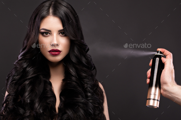 Beautiful brunette model: curls, classic makeup and red lips with a bottle of hair products.