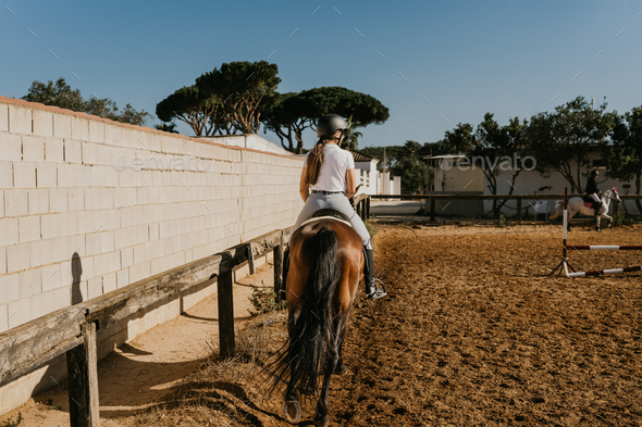 rear view of a woman rider warming up with her horse around the equestrian arena.