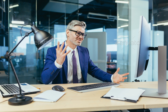 Angry and upset boss businessman shouting at computer monitor, man with glasses