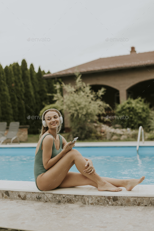 Young woman sitting by the swimming pool and listen music from mobile phone