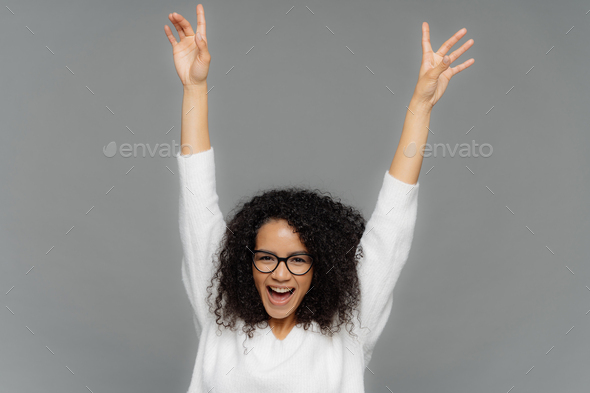 Happy pleased young woman raises hands up, being in high spirit