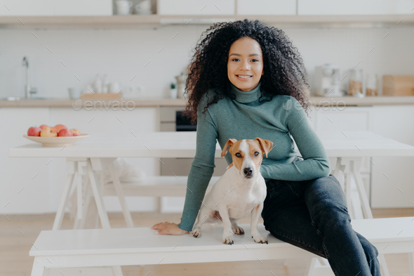Happy housewife with Afro haircut, sits at bench with pedigree dog