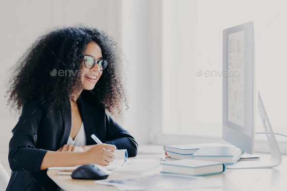 Professional curly haired woman manager makes report, focused into screen