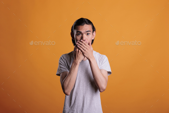Young man covering mouth with hands, speak no evil