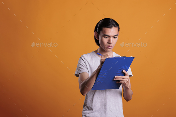 Young man taking notes in clipboard, writing in notepad