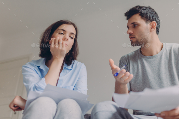 serious female and male do paperwork together, review bank documents and hold pen