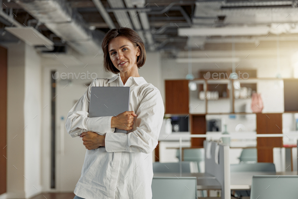 Attractive european business woman in casual clothe with laptop standing in modern office