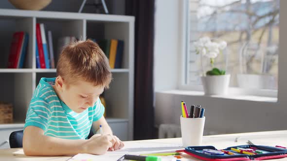 Boy is Doing  Homework at the Table. Cute Child is Learning at Home. alt